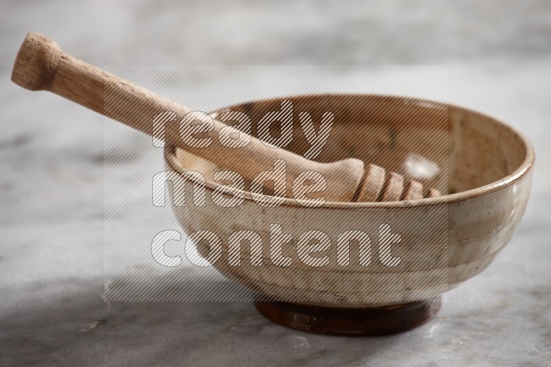 Beige pottery bowl with wooden honey dipper in it on grey marble background