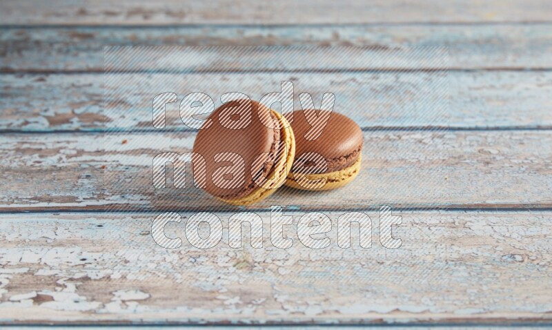 45º Shot of two Yellow and Brown Chai Latte macarons on light blue wooden background