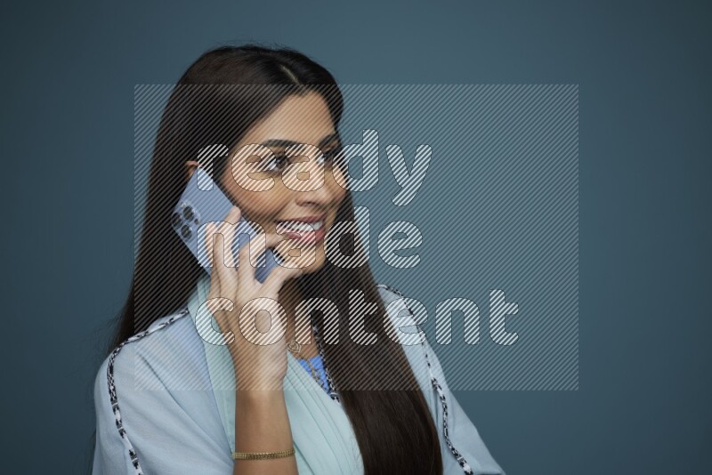 A Saudi woman having a Call in a blue background wearing a blue Abaya with no hijab