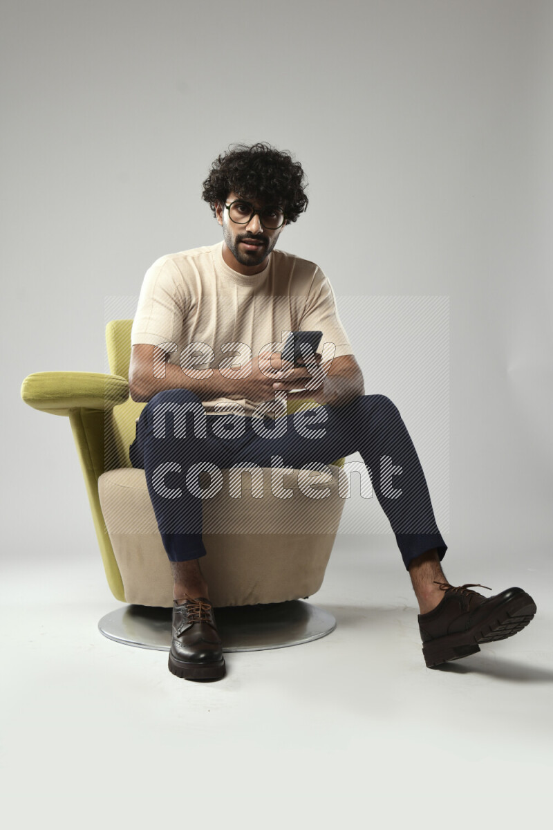 A man wearing casual sitting on a chair browsing on the phone on white background