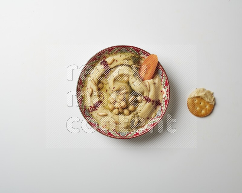 Hummus in a red plate with patterns garnished with zaatar & sumak on a white background