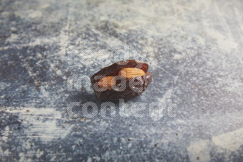 one almond stuffed madjoul dates on a rustic blue background