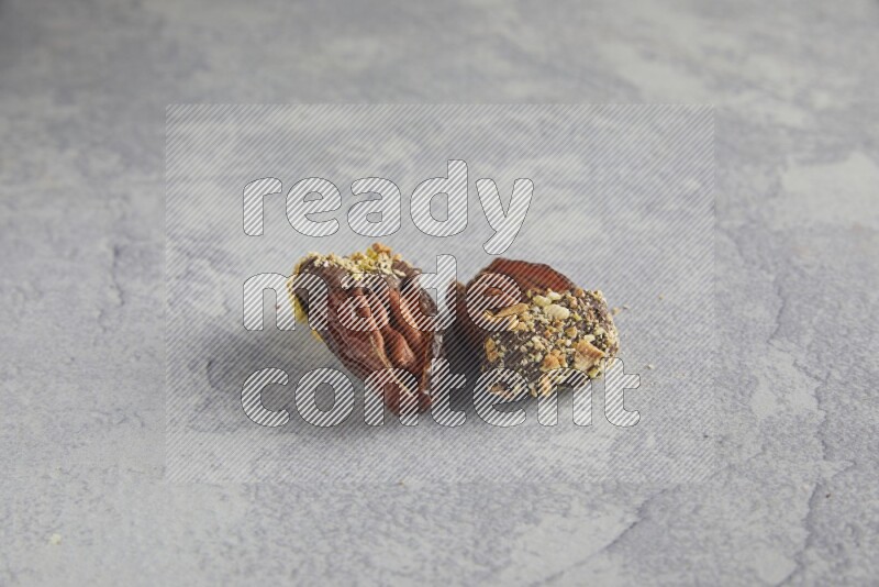 Two pecan stuffed dates covered with Dark chocolate and chopped pistachios on alight grey background