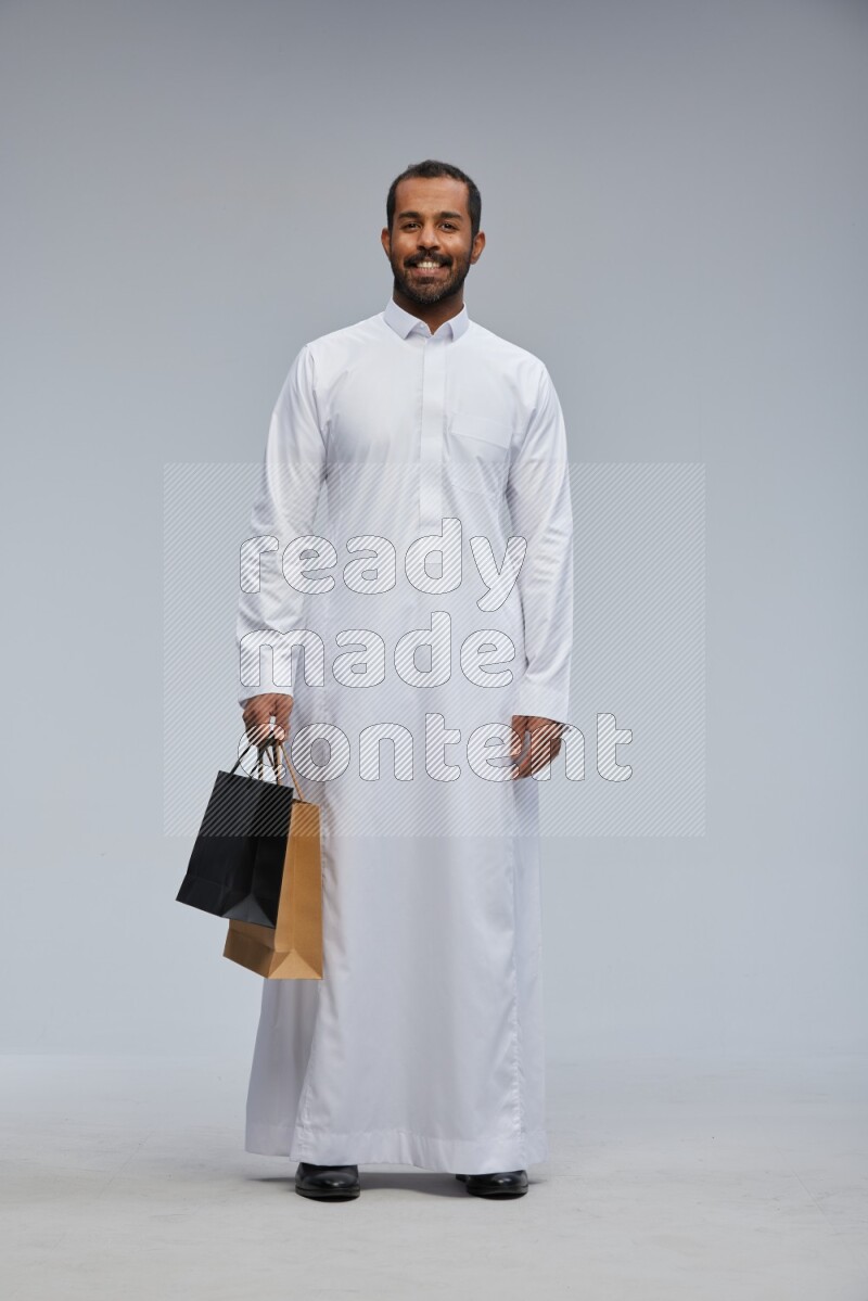 Saudi man Wearing thob standing holding shopping bag on Gray background