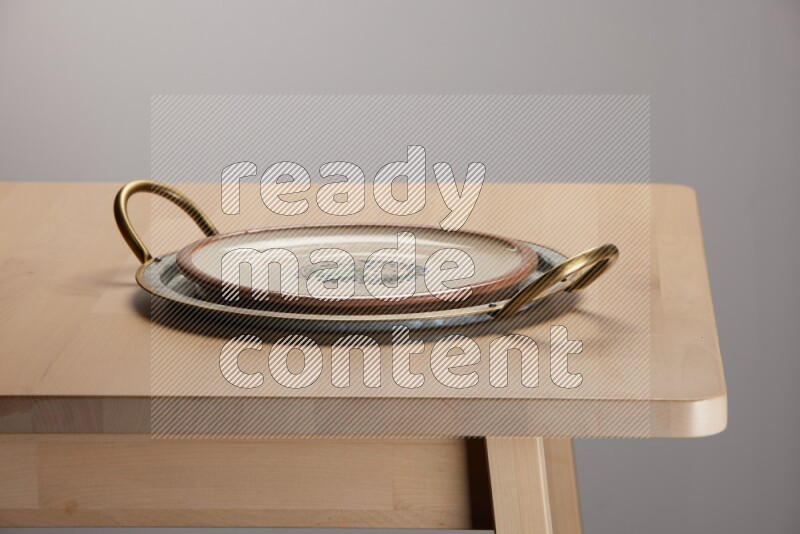 multicolored plate placed on a rounded stainless steel tray with golden handels on the edge of wooden table