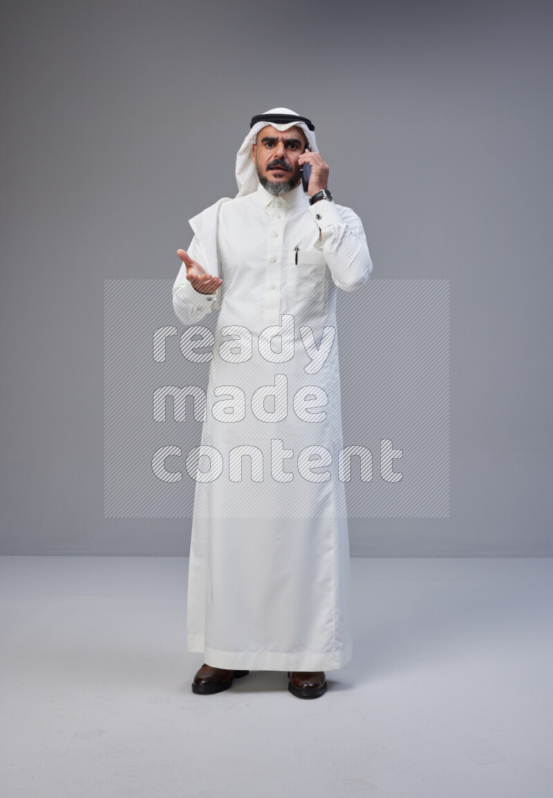 Saudi man Wearing Thob and white Shomag standing talking on phone on Gray background