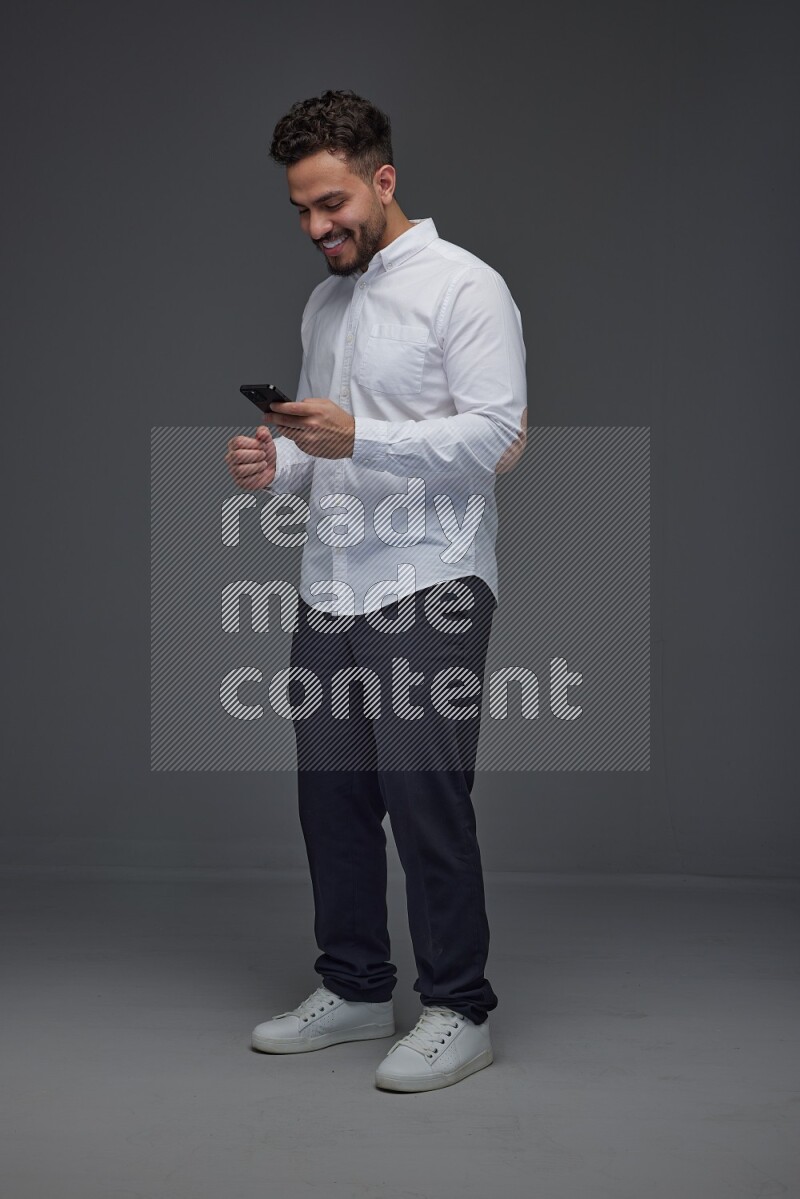 A man wearing smart casual standing and using his phone eye level on a gray background