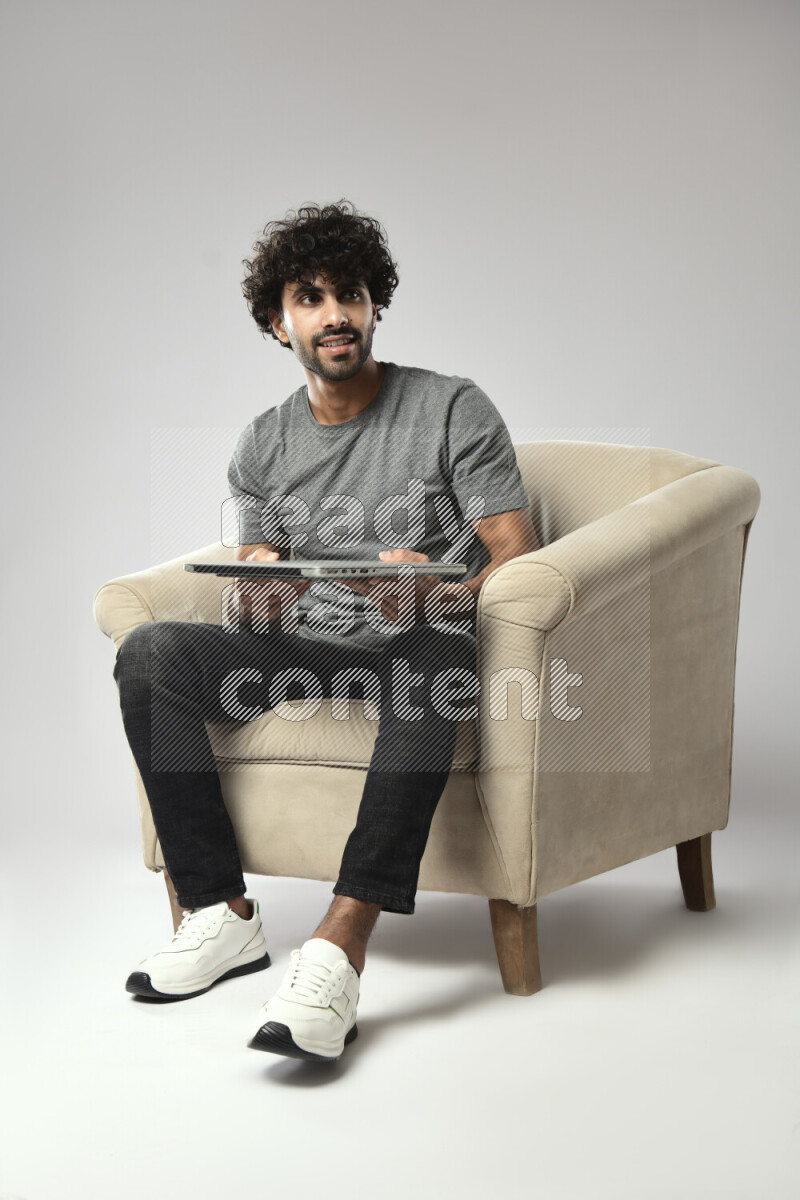 A man wearing casual sitting on a chair holding a laptop on white background