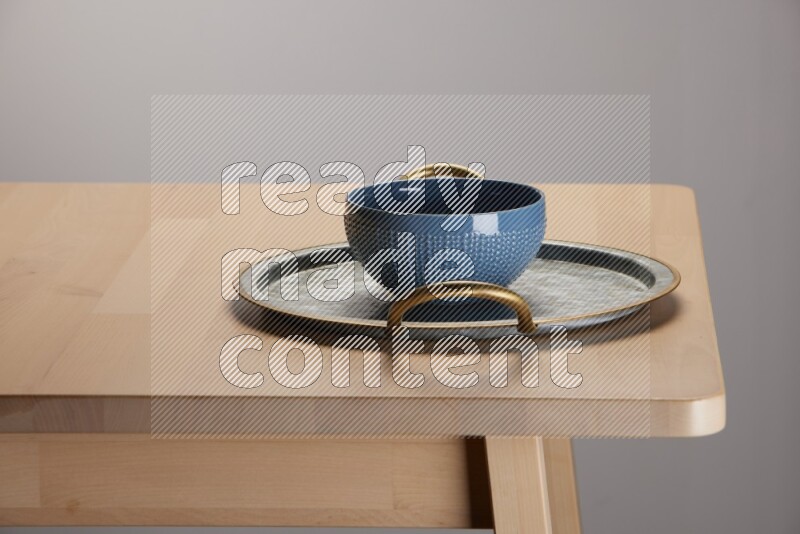 blue bowl placed on a rounded stainless steel metal tray with golden handels on the edge of wooden table