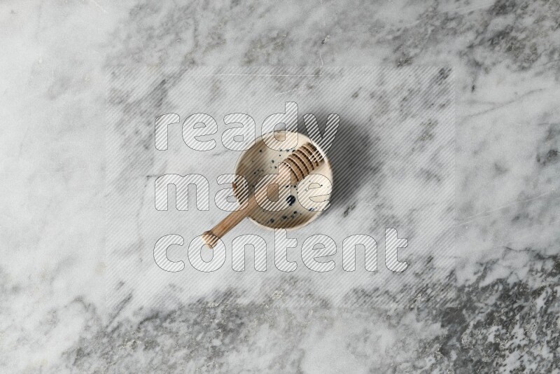Multicolored pottery bowl with wooden honey dipper in it on grey marble background