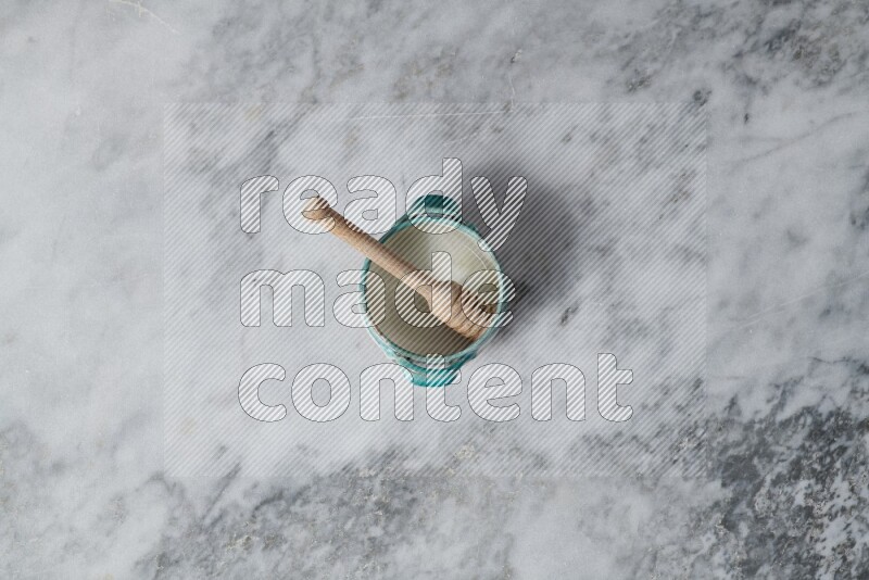 Multicolored pottery bowl with wooden honey dipper in it on grey marble background