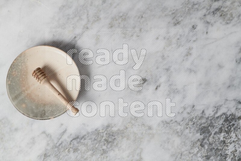 Multicolored pottery plate with wooden honey dipper in it on grey marble background
