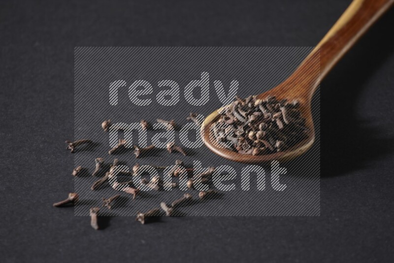 A wooden ladle full of whole cloves on a black flooring