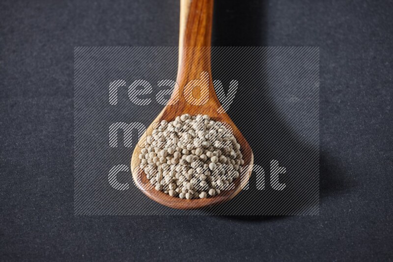 A wooden ladle full of white pepper beads on black flooring