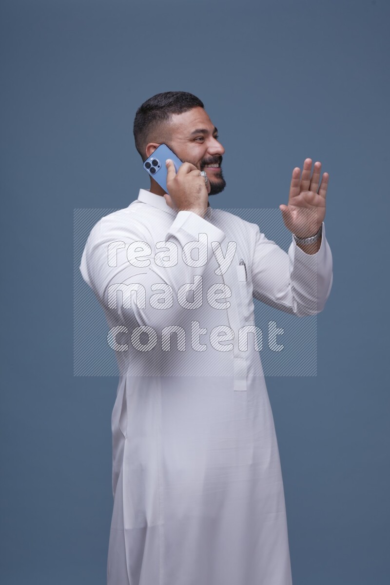 A Saudi man calling on blue background wearing Saudi Thob