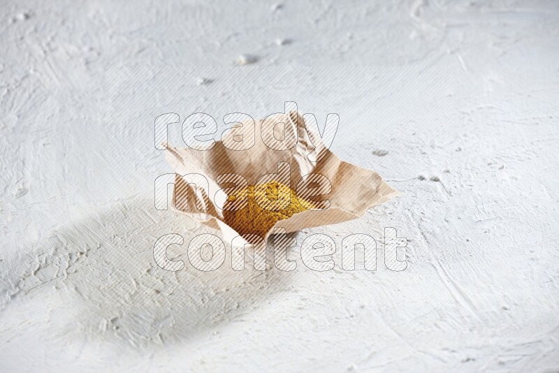 Turmeric powder in a crumpled piece of paper on textured white flooring