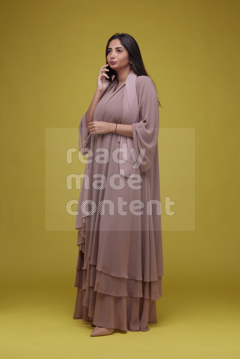 A woman Calling on a Yellow Background wearing Brown Abaya