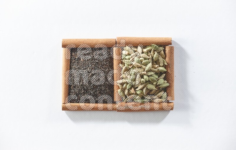 مربعان من أعواد القرفة ممتلئان بالشاي الأسود وحبوب الهال علي خلفية بيضاء