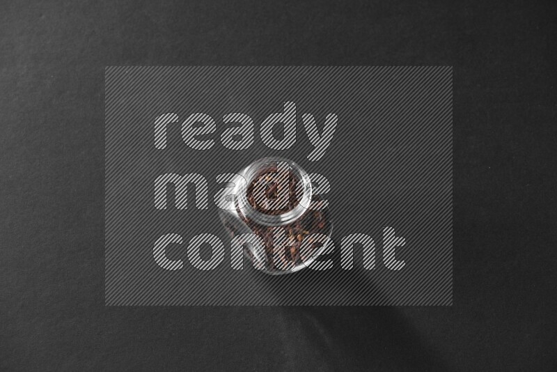 A glass spice jar full of cloves on black flooring
