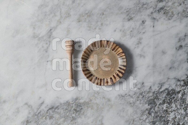 Multicolored pottery plate with wooden honey dipper on the side on grey marble background