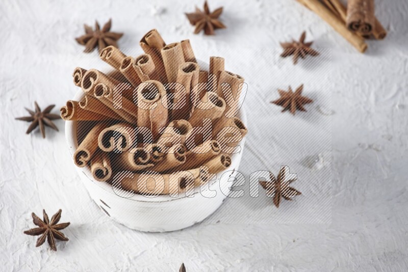 White bowl full of cinnamon sticks surrounded by star anis on a textured white background in different angles