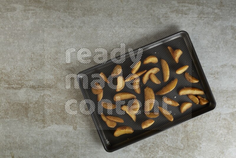wedges potato in a black stainless steel rectangle tray on grey textured counter top