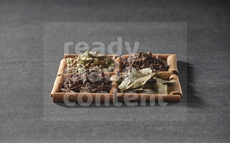 4 squares of cinnamon sticks full of star anise, cardamom, cloves and bay laurel leaves on black flooring