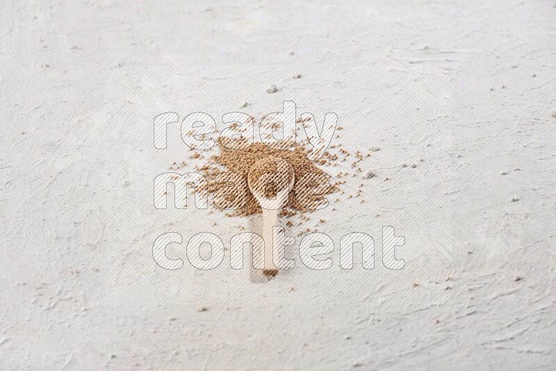 A wooden spoon full of mustard seeds on a textured white flooring