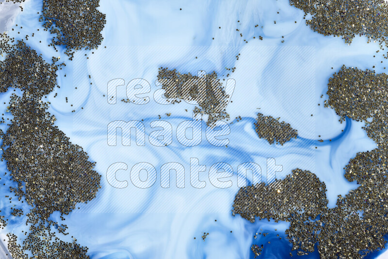 A close-up of sparkling gold glitter scattered on swirling blue background