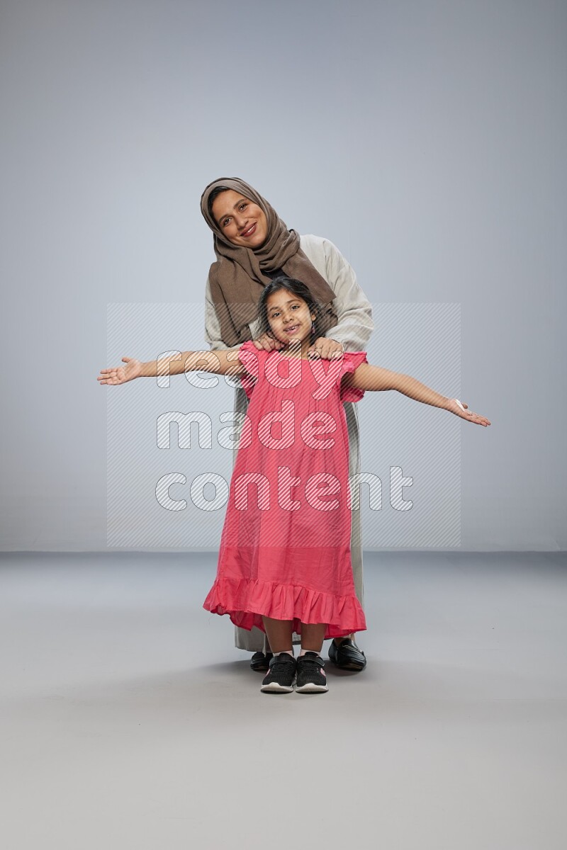 A girl and her mother interacting with the camera on gray background