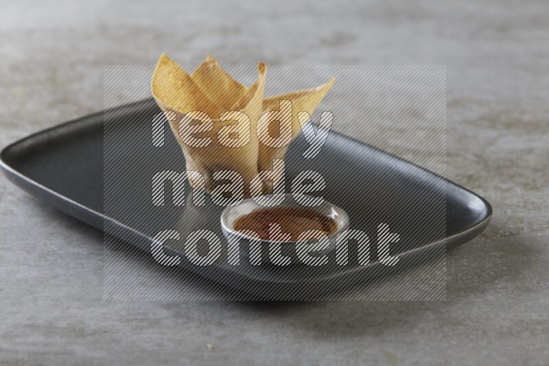 wonton cups with soy sauce ramkin on rectangle dark grey ceramic plate on grey textured counter top