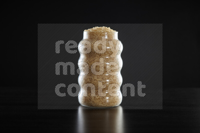 Basmati golden rice in a glass jar on black background