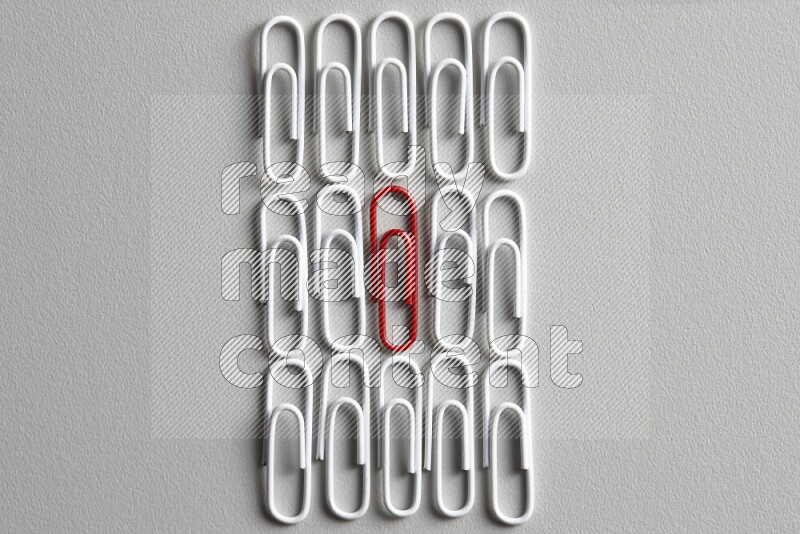 A bunch of white paper clips with a different colored paper clip in the center on grey background
