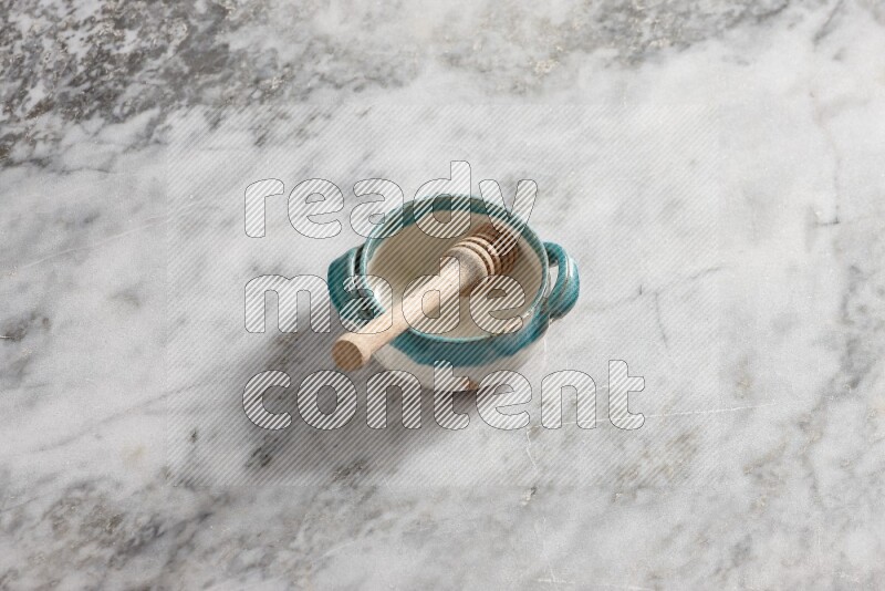 Multicolored pottery bowl with wooden honey dipper in it on grey marble background