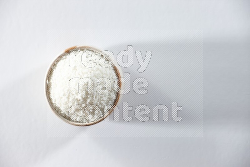 A beige ceramic bowl full of desiccated coconut on a white background in different angles