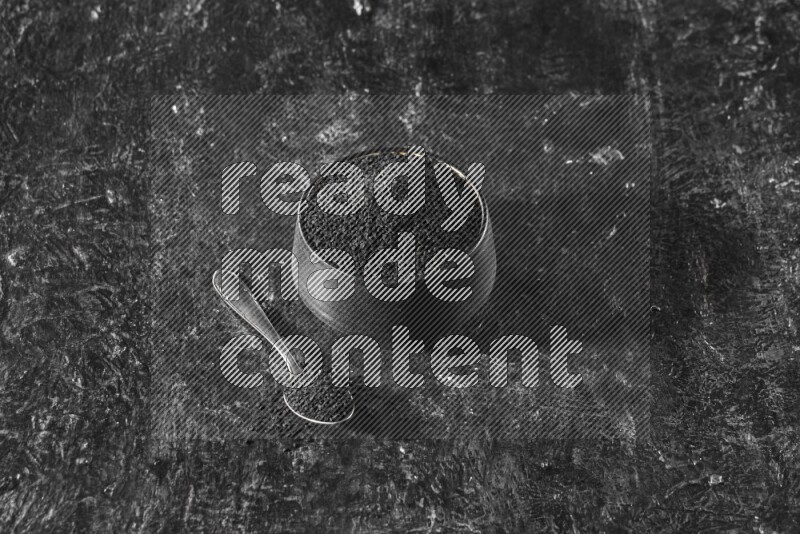 وعاء فخاري أسود وملعقة معدنية ممتلئان ببذور حبة البركة علي خلفية سوداء