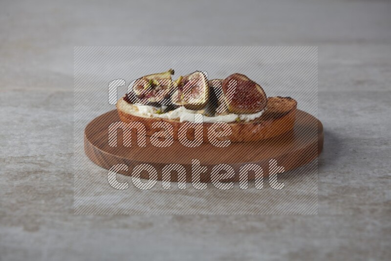 figs halves with cream cheese on toasted sourdough slice on a wooden board on textured grey background