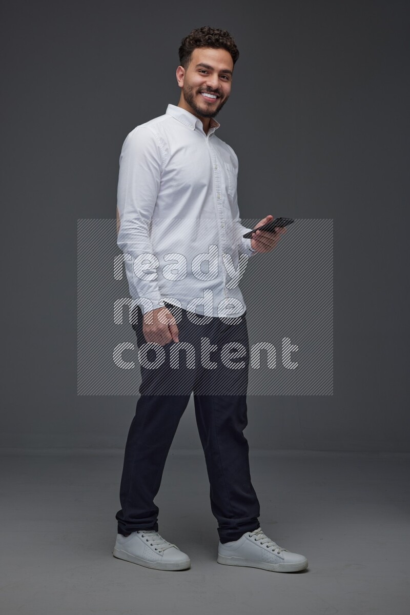 A man wearing smart casual standing and using his phone eye level on a gray background