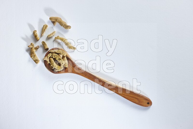 مغرفة خشبية مليئة بأصابع الكركم المجففة على خلفية بيضاء