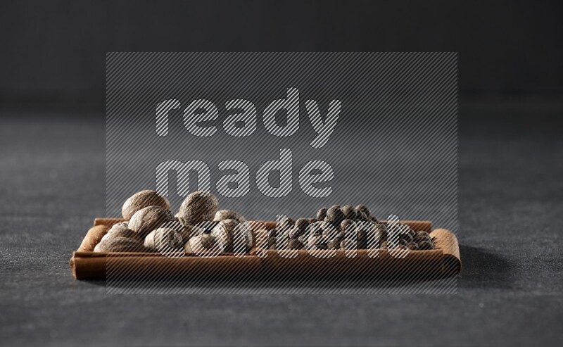 مربعان من أعواد القرفة ممتلئان بجوزة الطيب وحبوب الفلفل الحلو علي خلفية سوداء