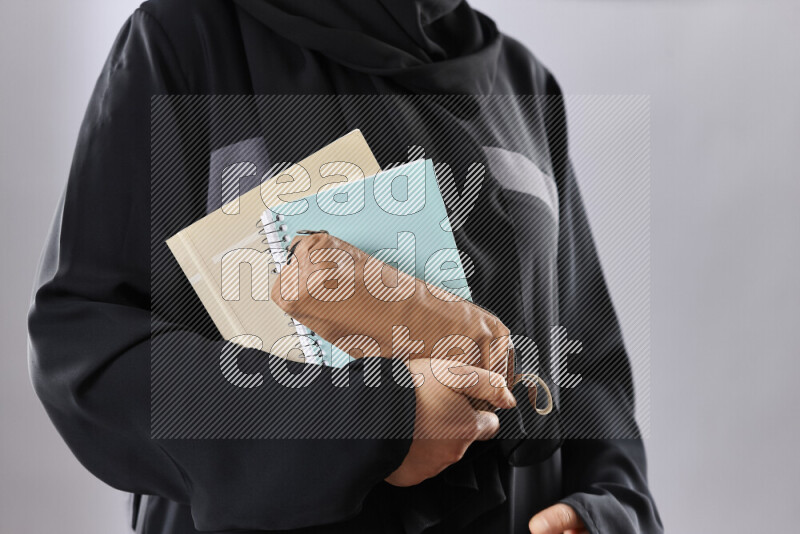 A woman in abaya holding books and a board in different positions (back to school)
