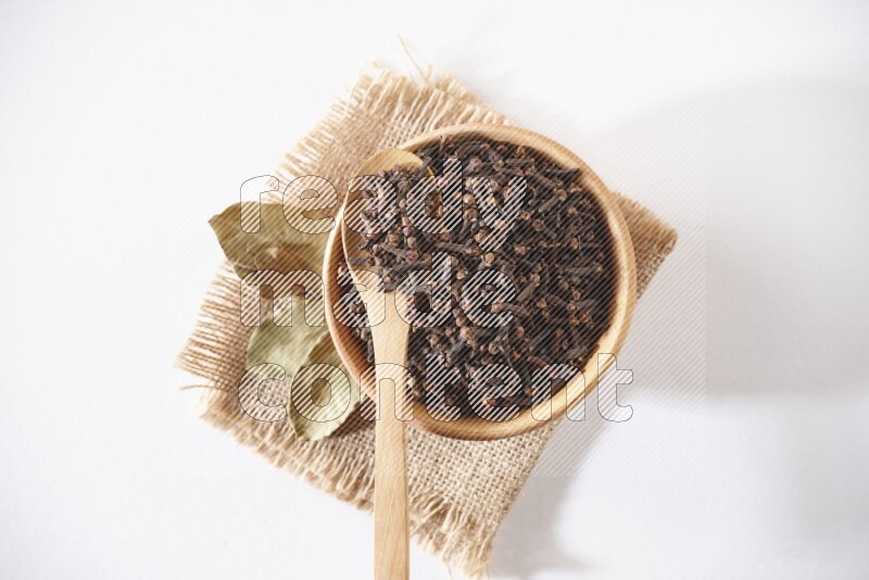 وعاء وملعقة خشبية ممتلئان بحبوب القرنفل علي قطعة من القماش علي خلفية بيضاء