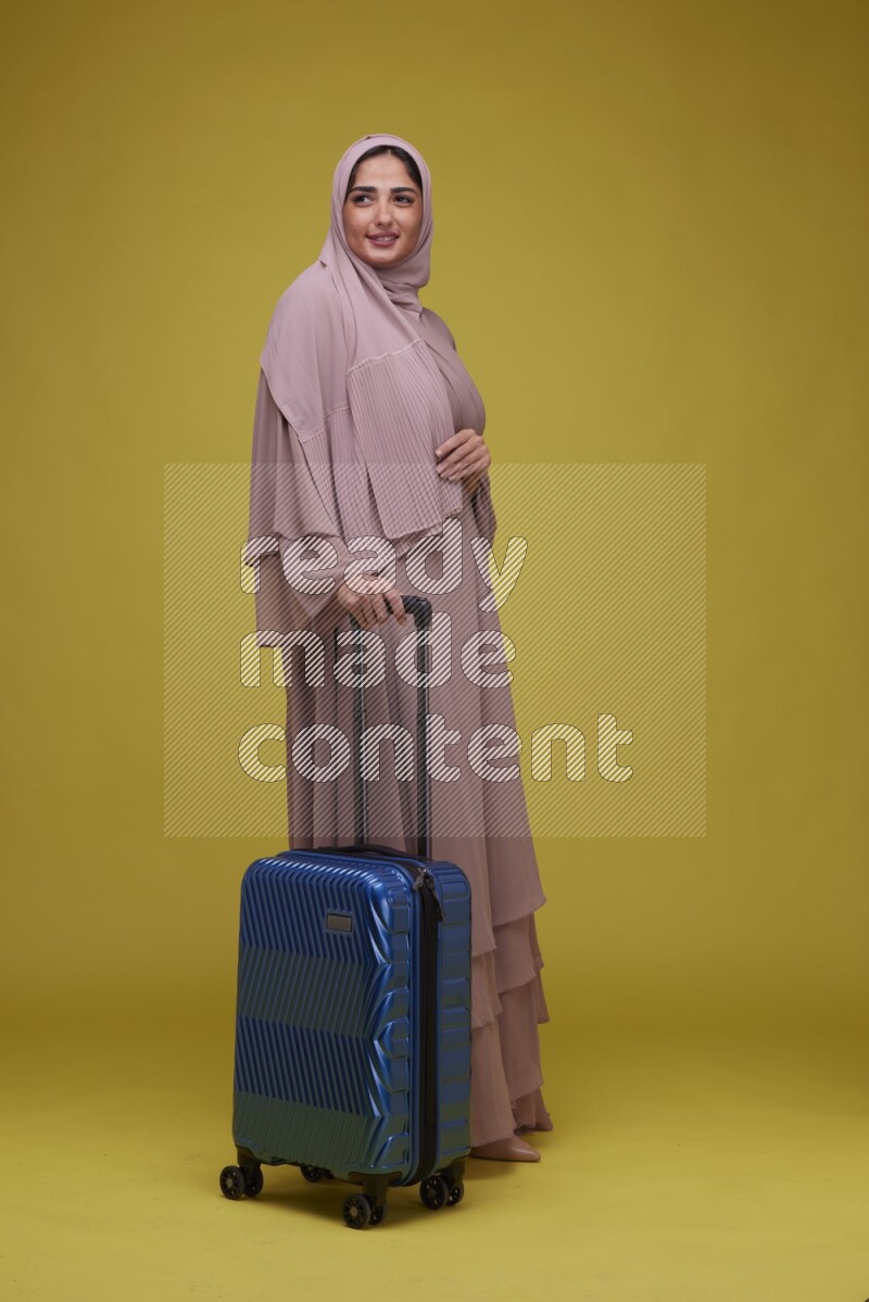 A woman With suit Case on a Yellow Background wearing Brown Abaya with Hijab