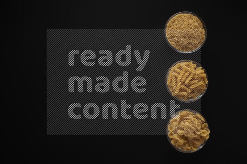 Different pasta types in 3 glass bowls on black background