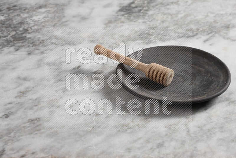 Black pottery plate with wooden honey dipper in it on grey marble background