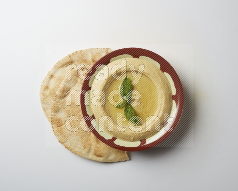 Hummus in a traditional plate garnished with mint on a white background