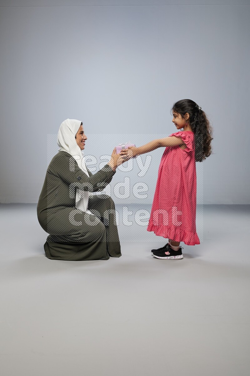 A girl giving a gift to her mother on gray background