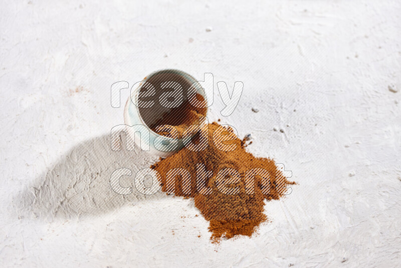 A colored pottery bowl full of ground paprika powder with fallen powder from it on white background