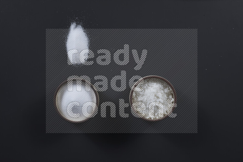 Pottery bowl full of fine table salt and coarse sea salt on black background