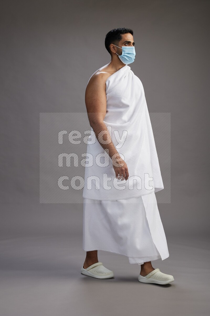 A man wearing Ehram with face mask Standing Interacting with the camera on gray background